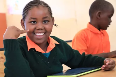 Girl with intellectual disability smiling while using a tablet in the classroom.