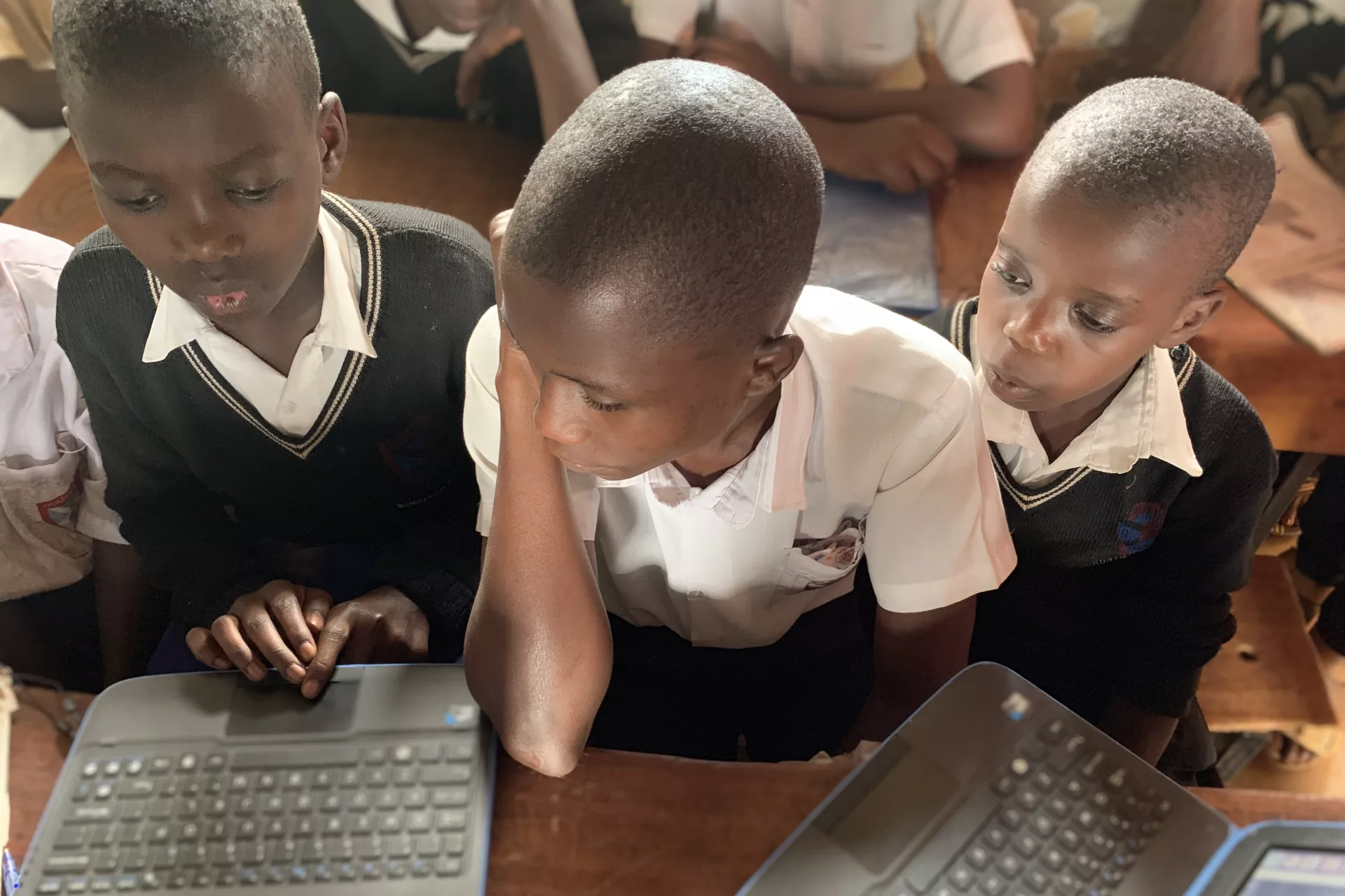 Three boys in a school in Uganda using laptops