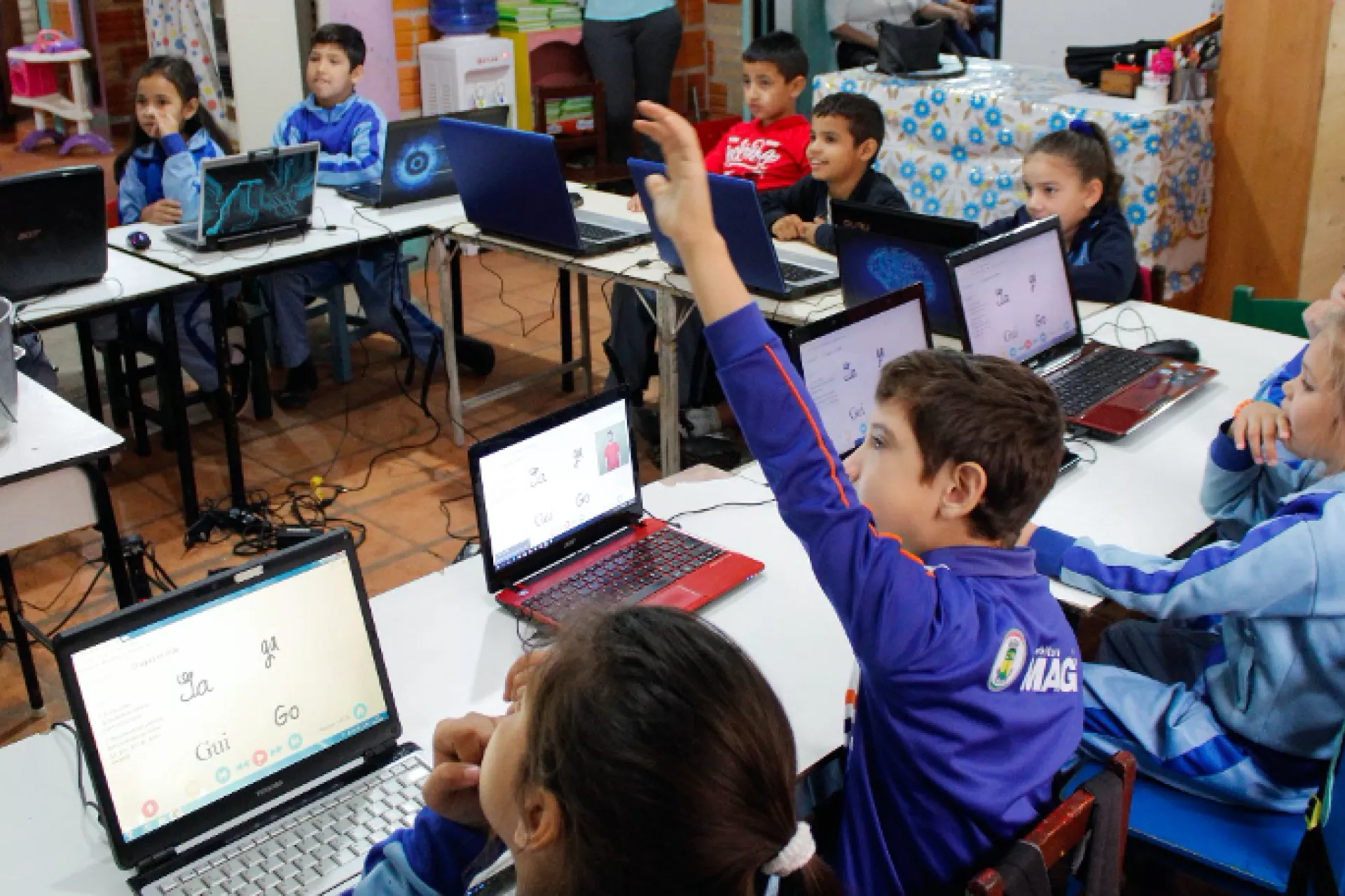 Classroom with children on laptops using the ADT, one child raises his hand.