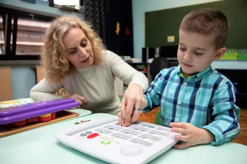 Young boy using assistive technology with the help of a teacher